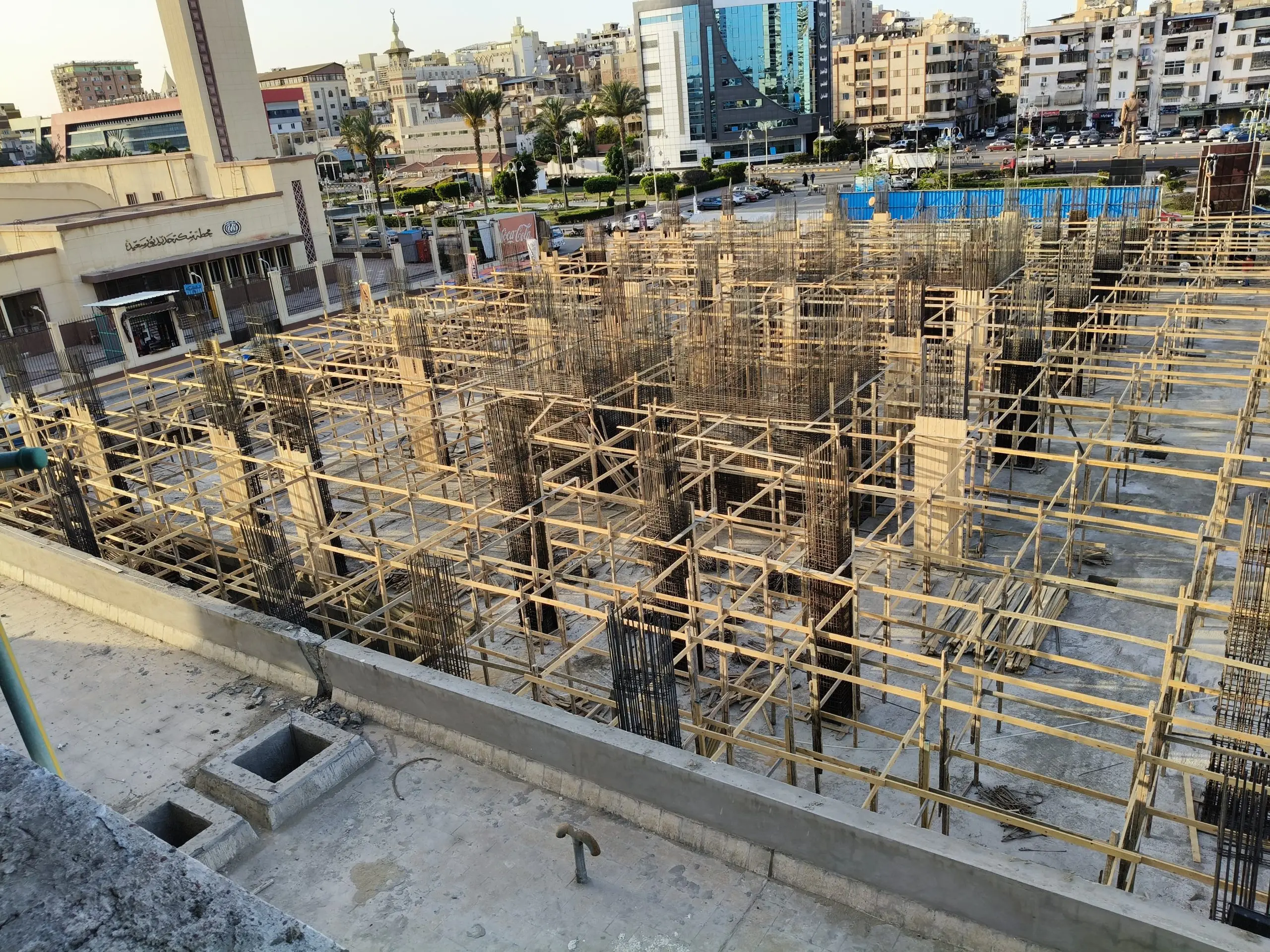 Concrete foundation reinforcement with wooden formwork at DiamoNest Tower city construction zone – أساسات خرسانية مع حديد تسليح وشدات خشبية في موقع بناء برج ديامونيست بالمدينة.