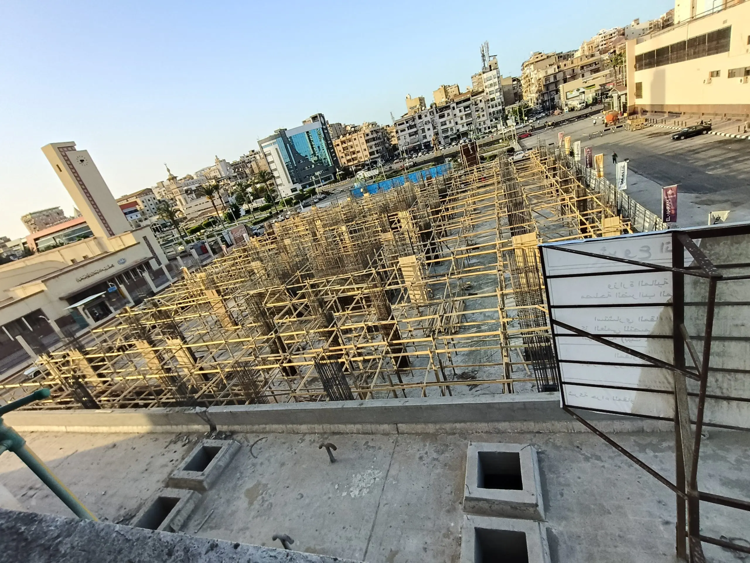 Concrete columns at DiamoNest Tower construction project in downtown with urban surroundings – أعمدة خرسانية في مشروع برج ديامونيست وسط المدينة مع المباني المحيطة.