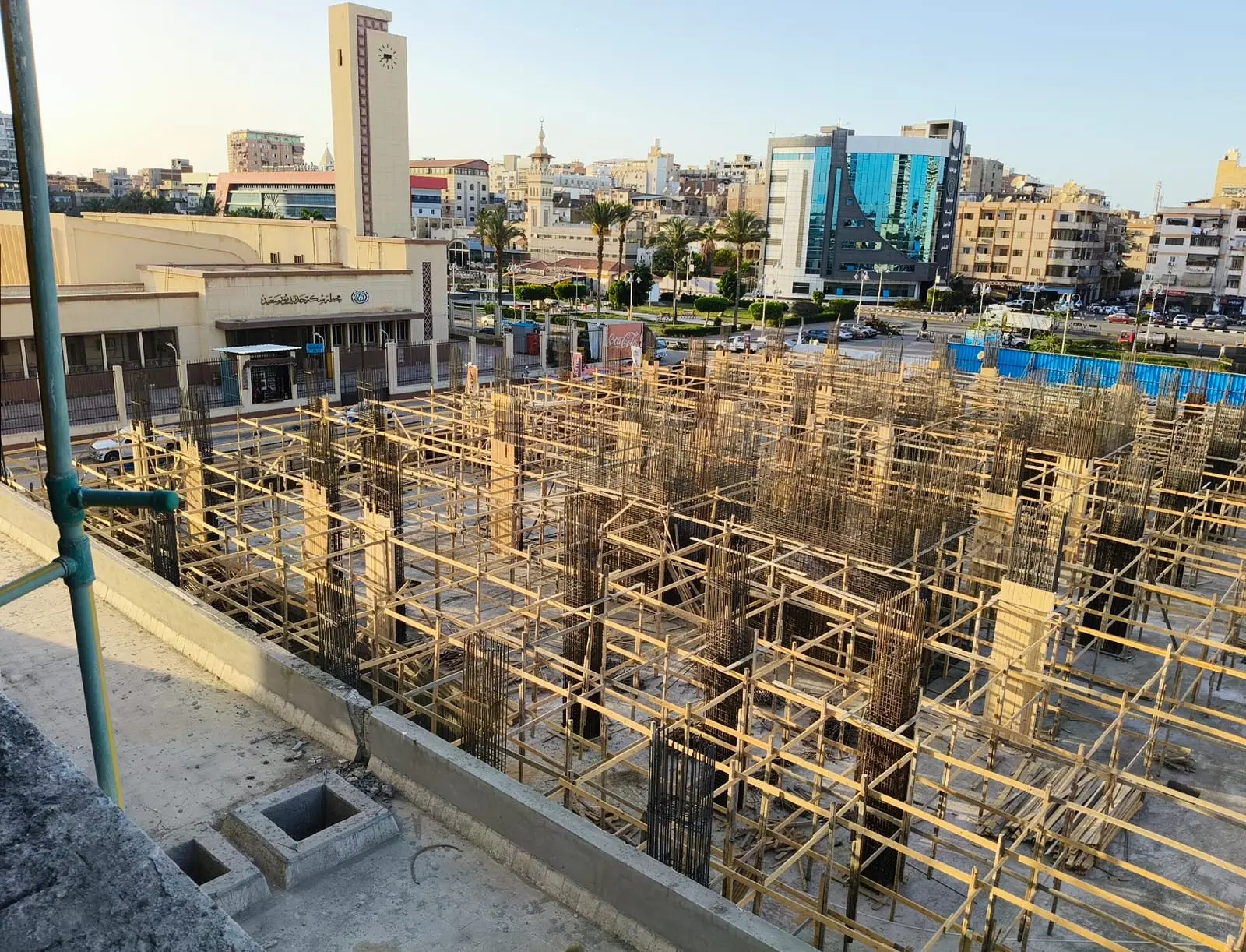 Column rebar and timber formwork at DiamoNest Tower construction site near urban buildings – حديد تسليح الأعمدة وقوالب خشبية في موقع برج ديامونيست قرب المباني الحضرية.